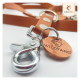 Nahaufnahme einer braunen Leder-Haustierleine mit silberner Hardware, mit einem runden Anhänger, der mit "WILDFANG" und einem Wolf-Logo geprägt ist.