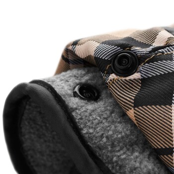 Nahaufnahme einer Haustierjacke mit einem karierten Muster in Beige und Schwarz, mit schwarzen Druckknöpfen und einem weichen grauen Futter.