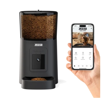 Schwarzer ZEDAR automatischer Haustierfutterspender mit Kamera und Trockenfutter, daneben eine Hand, die ein Smartphone zeigt, auf dem die ZEDAR A900 App mit einer fressenden Katze zu sehen ist.