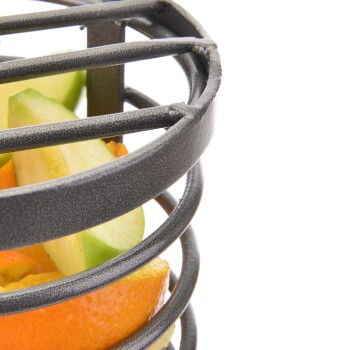 Eine Nahaufnahme eines metallenen Obsthalters mit Scheiben von Orange, grünem Apfel und gelber Paprika, die lebendige Farben zeigt.