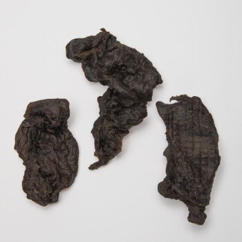 Drei Stücke dunkler, getrockneter Fleischleckereien für Haustiere, die eine faltige Textur und unterschiedliche Formen zeigen.
