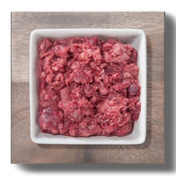 Quadratische weiße Schale mit rohem, zerkleinertem rotem Fleisch (rohes Tierfutter) auf einem Holzbrett.