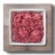 Quadratische weiße Schale mit rohem, zerkleinertem rotem Fleisch (rohes Tierfutter) auf einem Holzbrett.