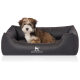 Ein kleiner, flauschiger Welpe sitzt bequem in einem dunkelgrauen Hundebett mit einem gesteppten Innenraum, das das Logo "KNUFFELWUFF" trägt.
