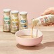 Hand gießt SmoothieCat Enten-Geschmack flüssigen Katzensnack in eine rosa Schüssel, mit Kaninchen-, Huhn- und Fischgeschmack in Flaschen.
