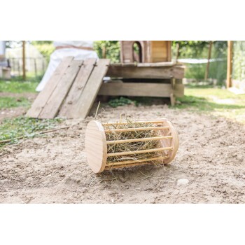 Ein hölzerner Heuballenfütterer, gefüllt mit Heu, liegt auf dem Boden in einem haustierfreundlichen Außenbereich, mit einem sichtbaren Holzhaustierhaus im Hintergrund.