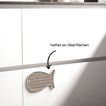 Ein dekorativer fischförmiger Magnet, der an einem weißen Schrank haftet, mit dem Text 'haftet an Oberflächen', der anzeigt, dass er an Oberflächen haftet.