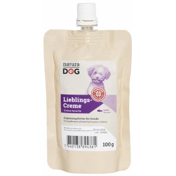Ein beiger Beutel mit Natura Dog Lieblings-Creme, einem Hundezusatz mit Lachs, mit einem lila Etikett und einer Cartoon-Hund-Illustration.