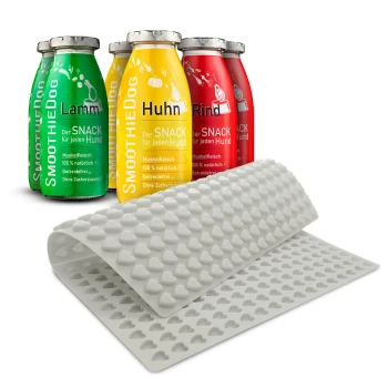 Vier bunte Smoothie-Flaschen für Hunde mit den Aufschriften "Lamm", "Huhn" und "Rind", neben einer rosa Silikonmatte mit Herzformen.