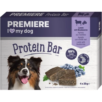 Eine Verpackung für Proteinriegel für Hunde mit einem lächelnden Hund, mit dem Text "PREMIERE I ❤️ meinen Hund Proteinriegel" und "69% Lamm mit Blaubeeren."