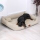 Ein schwarz-brauner Dobermann liegt bequem auf einem beigen Hundebett mit einem kleinen Kissen, vor einer hellen Wand und einem Holzboden.