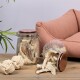 Zwei Glasbehälter gefüllt mit Haustierleckereien, einer umgekippt und verschüttet Leckereien, neben einem beigen Seilspielzeug und einem rosa Haustiersofa.