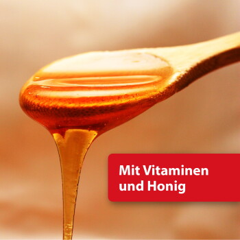 Goldener Honig, der von einem hölzernen Löffel tropft; rotes Schild mit dem Text „Mit Vitaminen und Honig”