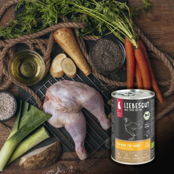 Dose Liebesgut Hundefutter mit Aufschrift 'Liebesgut - Bio-Huhn für Hunde' neben rohem ganzen Huhn, Karotten, Pastinake, Lauch und Samen.