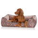 Ein goldbrauner Hund entspannt sich in einem bunten, gemusterten Tierbett mit geometrischem Design und zeigt seine entspannte Haltung und sein glänzendes Fell.