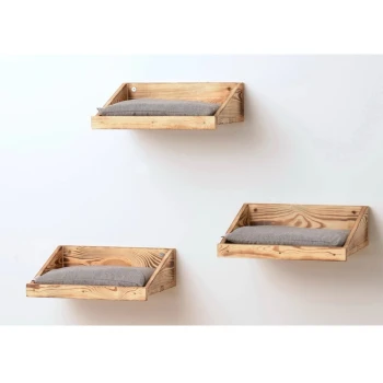 Drei hölzerne, wandmontierte Haustierbetten mit grauen Kissen, die in unterschiedlichen Höhen an einer weißen Wand angeordnet sind.