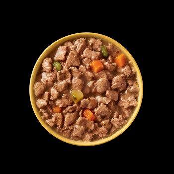 Kom met natte huisdiervoeding met stukjes vlees en kleurrijke groenten in een hartige jus, tegen een zwarte achtergrond.