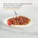 Tiernahrung auf einem weißen Teller mit zerkleinertem Fleisch, roten Stücken, einer Kirschtomate und dem Text: "Eine köstliche Kombination aus zwei Kreationen."
