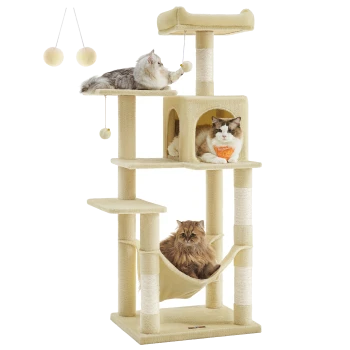 Drei Katzen spielen und entspannen auf einem beigen, mehrstöckigen Kratzbaum mit hängenden Spielzeugen, der einen gemütlichen Rückzugsort und eine Hängematte bietet.