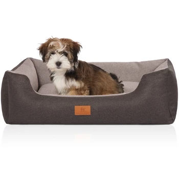 Ein kleiner, flauschiger Hund sitzt bequem in einem stilvollen, zweifarbigen Haustierbett mit einem braun-grauen Design, mit einem Lederetikett, das "KNUFFELWUFF" liest.