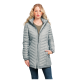 Eine Frau in einer hellgrauen Daunenjacke mit Kapuze, die mit den Händen in den Taschen steht, vor einem schlichten Hintergrund.