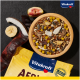 Eine Holzschüssel gefüllt mit buntem Vogelfutter-Mix, einschließlich Samen, getrockneten Früchten und Nüssen, neben einer gelben Vitakraft-Verpackung mit der Aufschrift 'AERIE.'