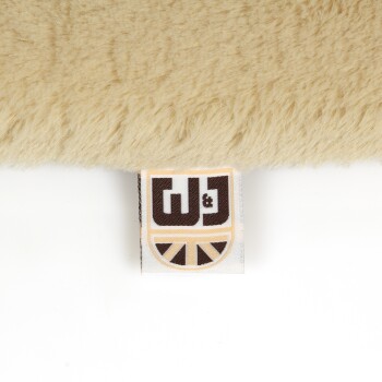 Nahaufnahme eines weichen, beigen Haustierbettes mit einem sichtbaren Etikett, das das Logo "W&J" in braunen und gelben Farben zeigt.
