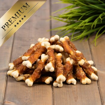 Ein Haufen hundeknochenförmiger Leckerlis mit braunem Äußeren und weißen Enden auf einer Holzoberfläche, mit grünem Gras im Hintergrund.