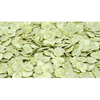 Nahaufnahme von hellgrünen, flachen Haustierfutterflocken, die über eine Oberfläche verstreut sind, um ihre Textur und Farbe zu zeigen.