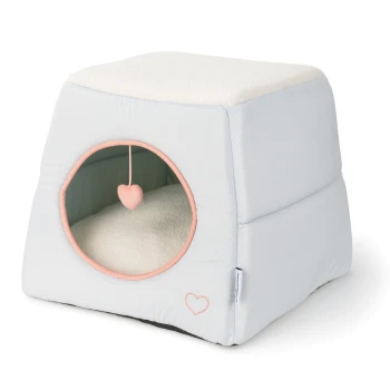 Przytulny domek dla zwierząt w jasnoniebieskim kolorze z miękkim białym wierzchem, z okrągłym wejściem i wiszącą zabawką w kształcie serca w środku.