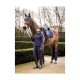 Ein Reiter in navyfarbener Reitkleidung steht neben einem braunen Pferd, beide mit passender blauer Ausrüstung, in einer üppigen Außenumgebung.