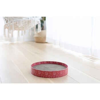 Ein runder Kratzpad für Katzen mit einem rosa gemusterten Rand, der verspielte Tierdesigns zeigt, auf einem hellen Holzboden platziert.