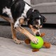 Ein verspielter Hund mit schwarz-braunem Fell interagiert mit einem grünen Spielzeugball mit braunen, pelzigen Beinen auf einem hellen Holzboden.