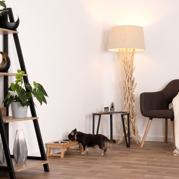 Ein kleiner brauner Hund, der aus einem Holz-Hundeschalenständer in einem modernen Wohnzimmer mit einer Stehlampe, einer Pflanze und dekorativen Regalen frisst.