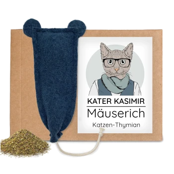 Blaues Filz-Mäusespielzeug mit Seilschwanz auf Karton, Haufen von Kräutern, Etikett zeigt Katze und Text 'KATER KASIMIR Mäuserich'.