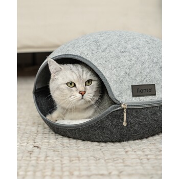 Ein gemütliches, rundes graues Katzenbett mit Reißverschluss, mit einer silbernen Tabbykatze, die herausblickt. Abmessungen: 46 cm x 38 cm x 26 cm.