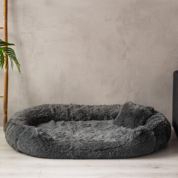 Gemütliches graues Haustierbett mit einem plüschigen, runden Design, vor einem minimalistischen Hintergrund mit einer nahegelegenen Bambuspflanze.
