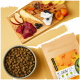 Eine Schüssel mit Trockenfutter für Haustiere neben einem Schneidebrett mit Rindfleisch, Apfelscheiben, Pastinake und Heidelbeeren, neben einer Tüte mit der Aufschrift "FAMILY PET FOOD."