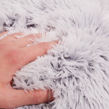 Eine Nahaufnahme einer Hand, die sanft in eine weiche, flauschige, grau-weiße Haustierdecke drückt und ihre plüschige Textur zeigt.