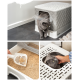 Eine graue Katze verlässt eine stilvolle Katzentoilette mit einem gesteppten Design. Die Box hat eine transparente Klappe und eine Schaufel daneben, die sauberen Katzenstreu zeigt.