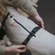 Eine Person, die einen schwarzen Riemen an einem hellbeigen Hundemantel anpasst, der eine Reißverschlusstasche und reflektierende Details aufweist.