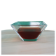 Eine klare Glasschüssel mit einer dunkelroten Flüssigkeit, auf einer hellen Holzoberfläche mit grünem Hintergrund platziert.
