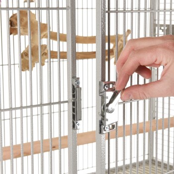 Eine Hand öffnet eine silberne Vogelkäfigtür mit einem Metallverschluss, der eine Holzstange im Inneren zeigt.