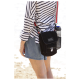 Eine Frau in einem gestreiften Hemd und Jeansshorts steht am Strand mit einer schwarzen DOOG-Tasche für Haustiere und einer Wasserflasche in der Netztasche.