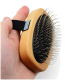 Eine Hand, die eine Holz-Haustierpflegebürste mit Metallborsten und einem schwarzen Griffband hält, vor einem weißen Hintergrund.