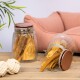 Zwei Glasbehälter gefüllt mit Hundeleckerlis, einer umgekippt, wobei lange, kaubare Sticks sichtbar werden. Im Hintergrund sind ein weiches rosa Haustierbett und ein Seilspielzeug zu sehen.