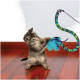 Chaton tigré gris sur un plancher en bois jouant avec une baguette à plumes bleues à manche vert-violet portant la marque "KONG".