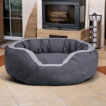 Graues rundes Haustierbett mit hellgrauem Rand, auf gefliestem Boden vor einem Kamin platziert.