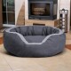 Graues rundes Haustierbett mit hellgrauem Rand, auf gefliestem Boden vor einem Kamin platziert.