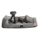 Ein schwarzer Hund mit einer weißen Brust ruht sich bequem auf einem plüschigen grauen Hundebett aus, das erhöhte Ränder zur Unterstützung hat.